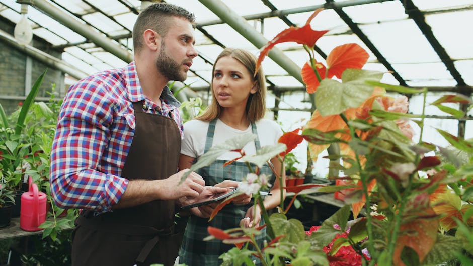 Two gardeners discussing plant care strategies with a digital tablet in a vibrant greenhouse setting.