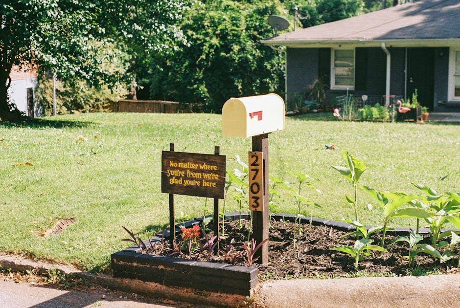Yellow mailbox with a warm welcoming sign and plants in a suburban front yard.